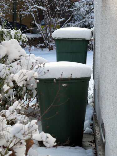 Due cisterne verdi per l'acqua piovana coperte di neve vicino al muro in inverno