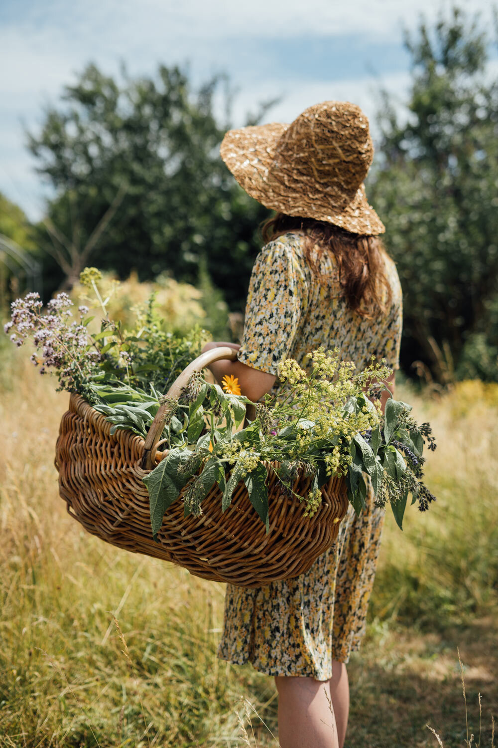 Donna con cappello di paglia che porta un cesto di vimini pieno di erbe e fiori appena raccolti
