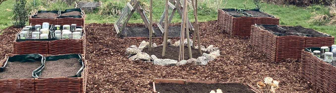 Giardino in primavera: aiuole rialzate intrecciate, sentieri di cippato e un sostegno di pali