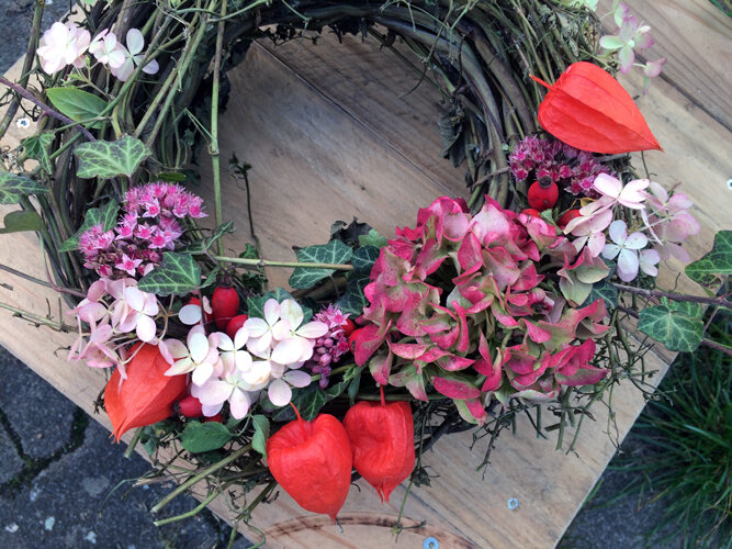 Ghirlanda autunnale fatta a mano con fiori rosa, alchechengi arancioni e foglie verdi
