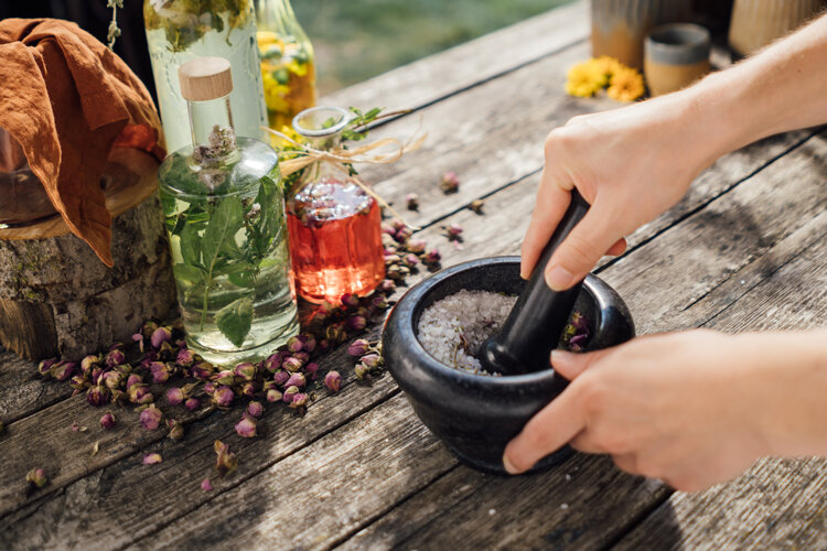 Sale alle erbe pestato nel mortaio, accanto olio aromatico e boccioli di fiori secchi