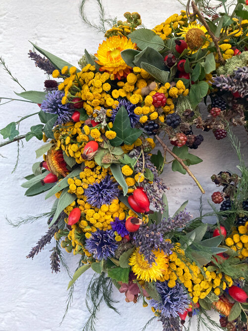 Dettaglio di una ghirlanda autunnale con fiori gialli e blu, cinorrodi rossi e bacche scure