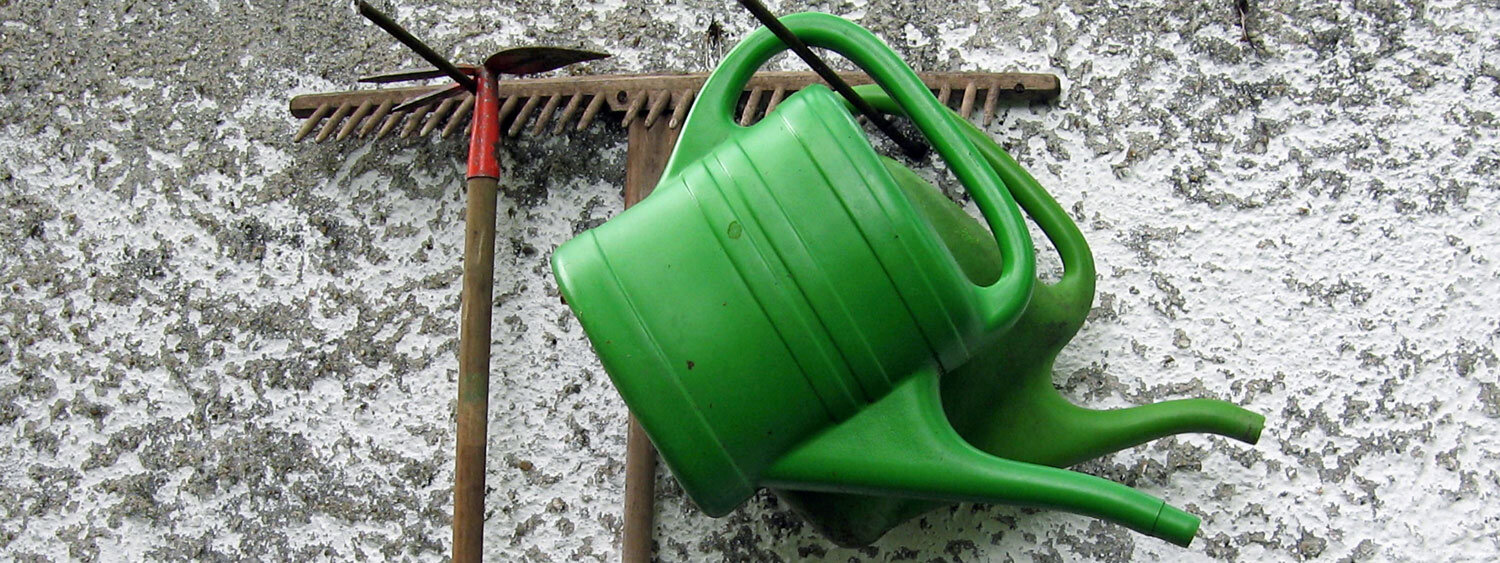 Due annaffiatoi verdi e un rastrello appesi a un muro