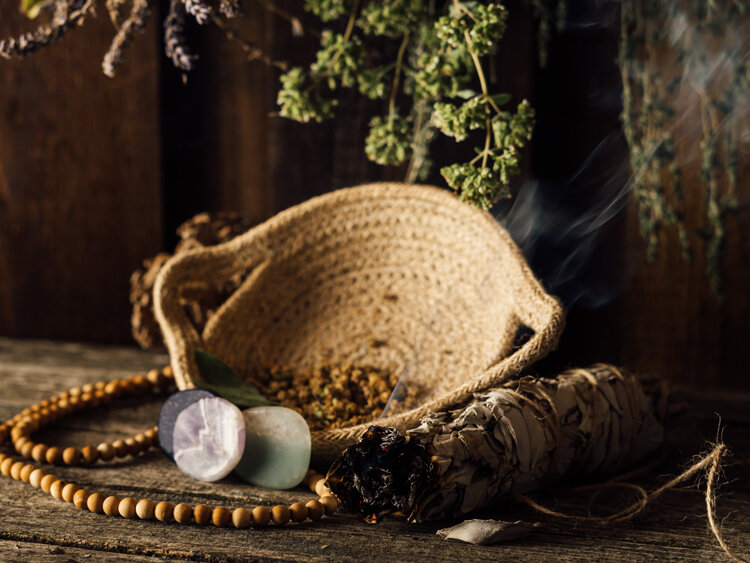 Mazzetto di salvia fumante accanto a una ciotola, pietre e una collana di perle di legno