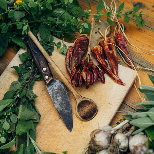Peperoncini essiccati, erbe fresche e aglio su un tagliere con coltello e cucchiaio di legno