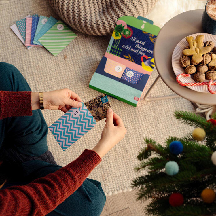 Persona che apre una bustina di semi del calendario dell'Avvento, accanto biscotti e un abete