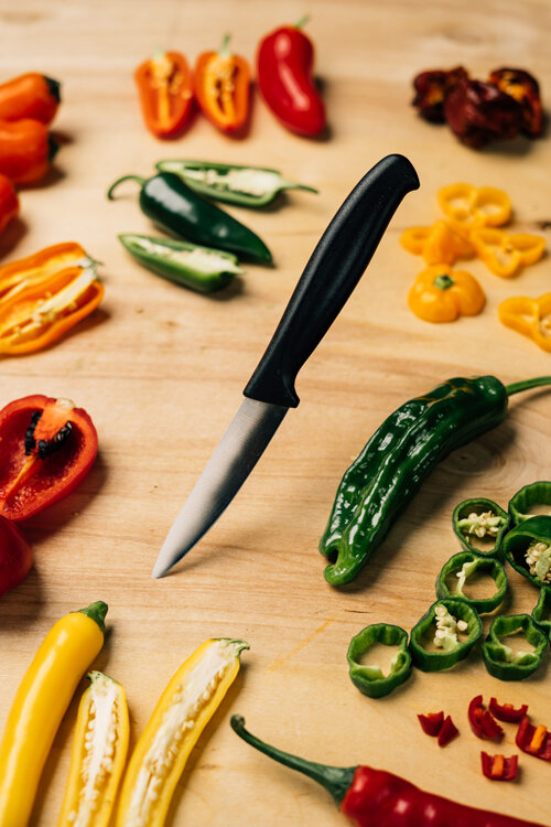 Peperoncini tagliati rossi, gialli, arancioni e verdi con un coltello su un tagliere